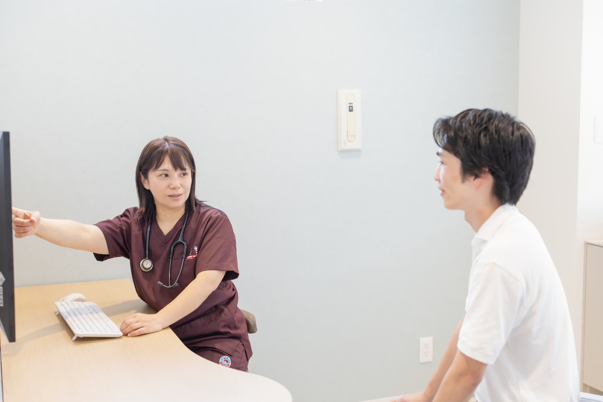 聴診器を着けた女性医師がモニターを指し示しながら患者に説明する診察風景