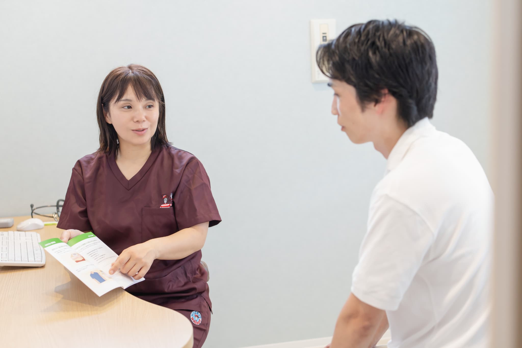 パンフレットを使って男性患者に治療内容を説明する女性医師の診察風景