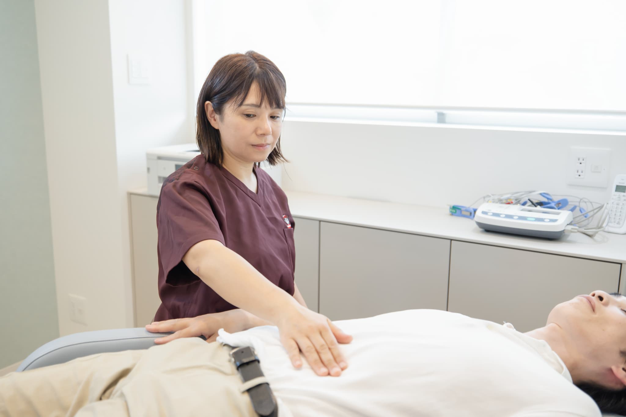 女性医師がベッドに横たわる患者の腹部に手を当てて触診を行う様子