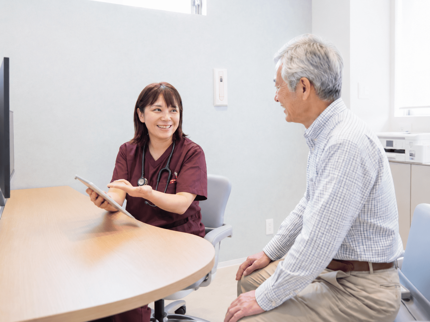 女性医師がタブレットを手に高齢の男性患者へ検査結果を説明する様子