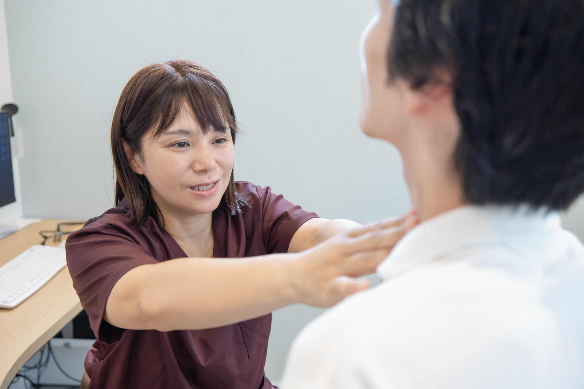 女性医師が患者の首元に手を当てて甲状腺の触診を行う様子