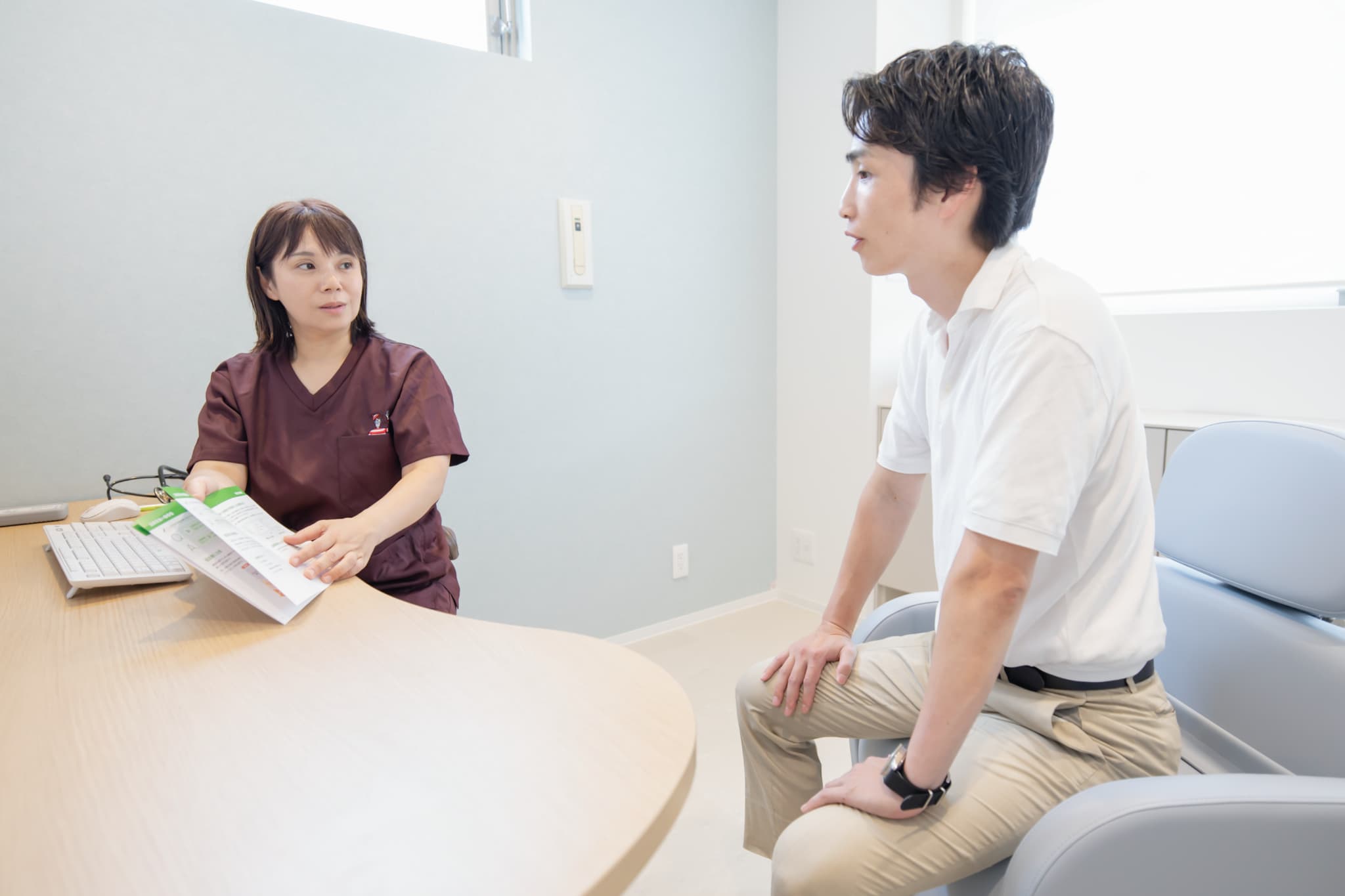 女性医師がパンフレットを手に男性患者と向き合って診察・相談を行う様子